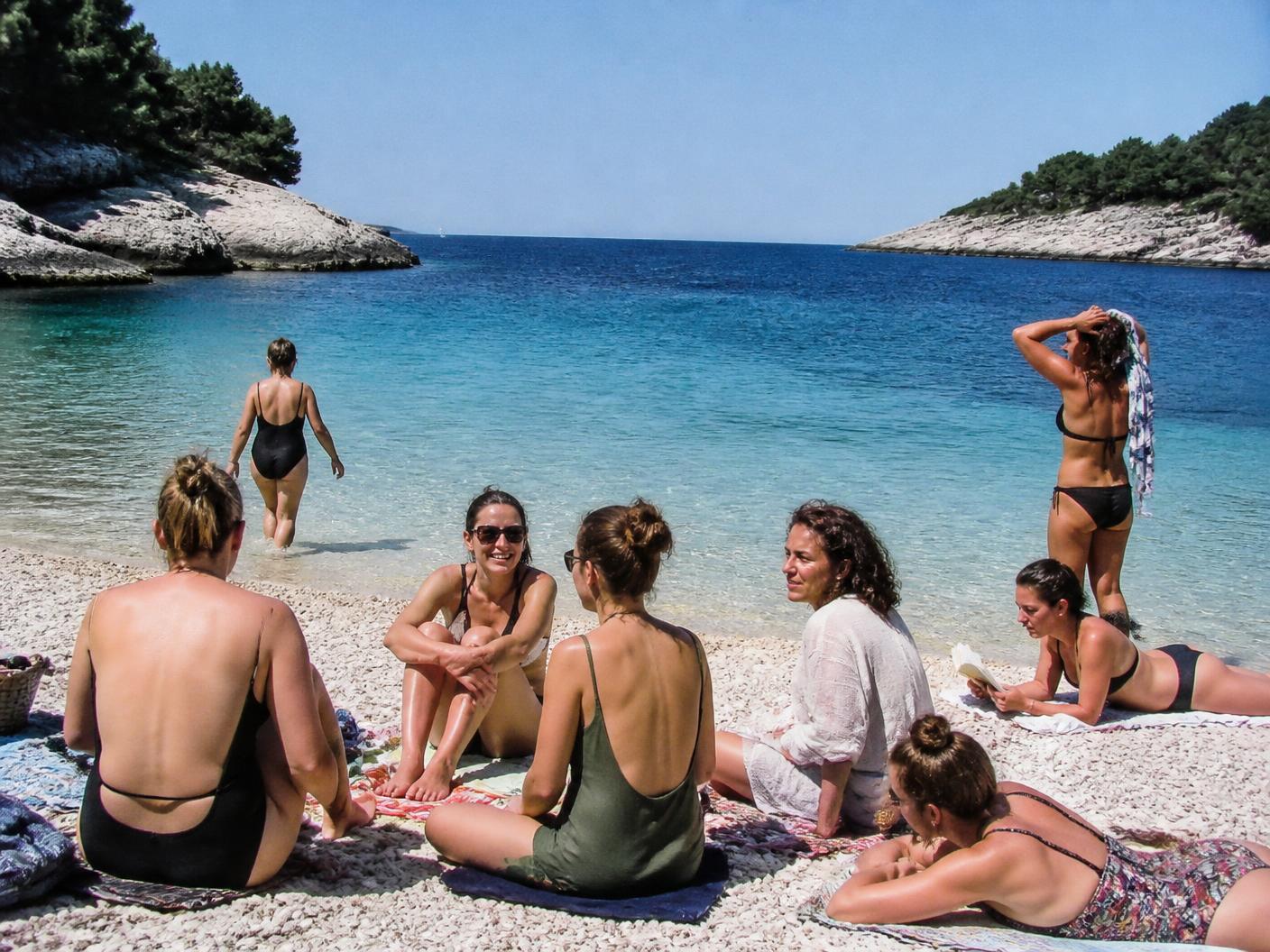 Women resting by clear turquoise Adriatic water on an empty rocky Istrian shore in September
